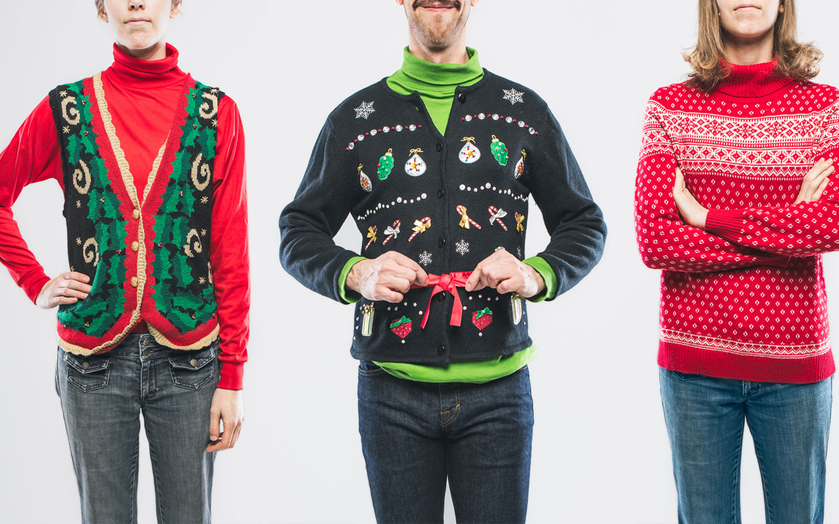 An image of a group of people wearing knit ugly Christmas sweaters with various bizarre patterns and decorations.