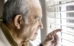 Pensive senior man looking through a window isolating form Covid virus.