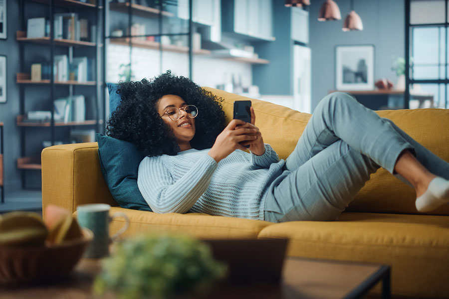 Woman laying on a couch using a phone to text.